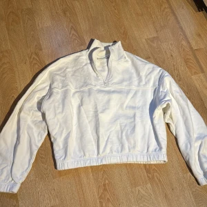 Vit tröja med dragkedja från Weekday - Säljer en superfin vit tröja från Weekday i storlek XS. Den har en halv dragkedja framtill och är gjord i ett mjukt material som känns skönt mot huden. Perfekt för en avslappnad stil och passar bra till både jeans och kjol. Tröjan är i nyskick och redo för nya äventyr!