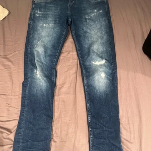 Blå jeans från Antony Morato - Säljer ett par snygga blå jeans från Antony Morato. De har en cool distressed look med slitningar på benen. Perfekta för en avslappnad stil. Passar bra till både vardag och fest!