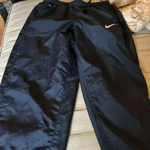 Säljer ett par mörkblåa träningsbyxor från Nike. De är i bra skick och perfekta för träning eller en avslappnad dag. Byxorna har en elastisk midja och en liten Nike-logga på sidan. Superbekväma och stilrena!