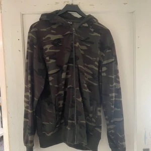 Camouflage hoodie från Origin's Paris - Säljer en snygg camouflage hoodie från Origin's Paris i storlek M. Den har en dragkedja framtill och är perfekt för höst och vår. Materialet känns mjukt och bekvämt, och den har en klassisk huva. Perfekt för en casual look eller när du vill smälta in i naturen!