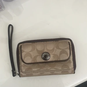 Plånbok från Coach - Säljer en snygga vintage plånbok från Coach med deras ikoniska mönster. Plånboken har dragkedja och många fack för kort!! Mått:  Bredd 16cm , höjd 10cm , djup 4cm