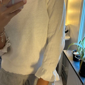 Vit tröja med volangdetaljer - Säljer en superfin vit tröja med volangdetaljer vid ärmslut och hals. Den är perfekt för både vardag och festliga tillfällen. Tröjan är trekvartsärmad och har en normal passform. Materialet känns mjukt och bekvämt, vilket gör den till ett måste i garderoben!