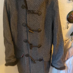 Grå kappa med pälskant - Säljer en superfin grå duffel med ett snyggt rutmönster. Den har en mysig pälskant vid huvan och coola knappar framtill. Insidan är fodrad med ett härligt rött tyg som ger en lyxig känsla. Perfekt för höst och vinter! st 2 från Odd Molly. aldrig använd 