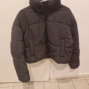 Svart pufferjacka - Säljer en svart pufferjacka som är perfekt för kyliga dagar. Jackan har en hög krage och dragkedja framtill. Den är quiltad och har långa ärmar för extra värme. Passar bra till både vardag och fest!