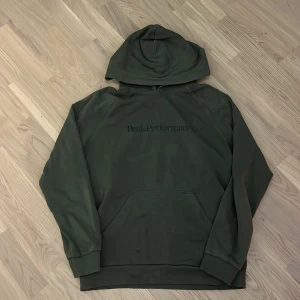 Grön hoodie från Peak Performance - Säljer en snygg och bekväm grön hoodie från Peak Performance. Den har en klassisk design med en stor ficka fram och en luva. Perfekt för både vardag och chill dagar. Passar bra till jeans eller träningsbyxor!