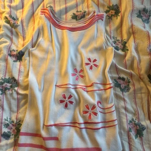Vit och rosa ärmlös topp - Säljer en söt vit ärmlös topp med rosa detaljer och blommönster. Toppen har en unik design med rosa ränder vid halsen och nederkanten. Perfekt för sommardagar! Vintage från dem tidiga 2000s. pris kan diskuteras 💗💗🎀