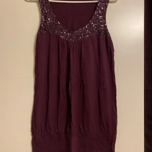 Mörklila tunika från Lindex - Säljer en snygg mörklila tunika från Lindex i storlek M. Den är ärmlös och har glittriga paljettdetaljer vid halsringningen. Perfekt för festliga tillfällen! 💜