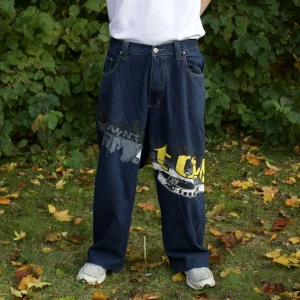 Y2K Baggy jeans - Säljer ett par coola baggy jeans med graffiti-inspirerat mönster i gult och vitt. De har en loose fit och är perfekta för en avslappnad streetwear-look. Jeansen är mörkblå och har klassiska femfickor. Perfekta för höst och vår!