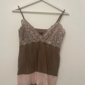 Sött brunt & rosa linne - Säljer en unik brun och rosa ärmlös topp med spetsdetaljer och blommigt mönster. Toppen har en v-ringad design och är perfekt för sommarens fester. Den är gjord i ett lätt och luftigt material som känns skönt mot huden. (En tightare M så skulle nog funka för S också!)