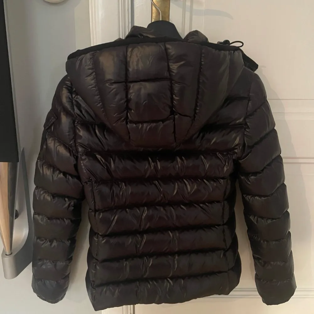 Säljer en snygg svart dunjacka från Moncler. Jackan är i nyskick och har en normal passform med långa ärmar. Den är perfekt för vintern med sitt quiltade mönster och dragkedja framtill. Huvan ger extra värme och stil. Perfekt för kalla dagar! ❄️. Jackor.