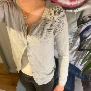 Hv polo kofta  - En jätte gullig grå kofta med coolt mönster på ena axeln i storlek xs, sparsamt använd utan större skador. 