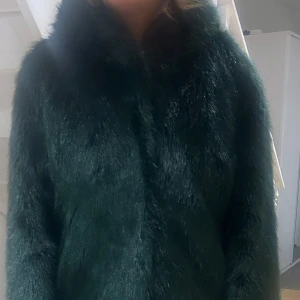Mörkgrön pälsjacka - Säljer en supermysig mörkgrön pälsjacka som är perfekt för kyliga dagar. Jackan har en elegant och fluffig look med långa ärmar. Den är både stilren och varm, vilket gör den idealisk för både höst och vinter. Passar perfekt till både vardag och fest!