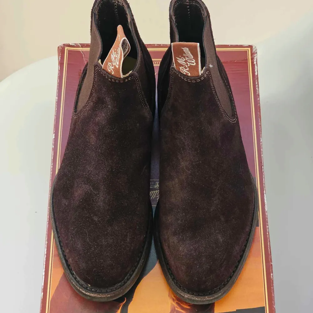 Säljer ett par snygga bruna mocka boots från R.M. Williams i mycket bra skick. De har en klassisk design med elastiska paneler på sidorna för enkel på- och avtagning. Perfekta för höst och vinter, och de ger en stilren touch till vilken outfit som helst.. Skor.