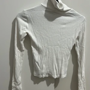 Vit ribbad polotröja från Sister - Säljer en stilren vit ribbad polotröja från Sister i storlek XXS. Perfekt för kyliga dagar med sin långa ärmar och mjuka material. Tröjan har en klassisk polokrage som ger en elegant touch. Passar både till vardags och festliga tillfällen.