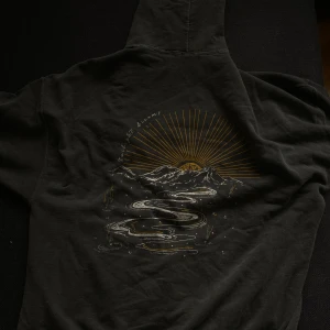 BAGGY/OVERSIZED HOODIE - Säljer en svart hoodie från Urban Outfitters med ett coolt solnedgångsmotiv på ryggen. Den har en känguruficka fram och en bekväm passform. Perfekt för höstkvällar eller som en stilren vardagströja. 🌄