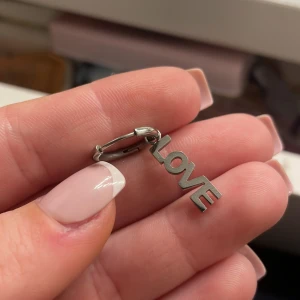 Silverörhänge från edblad - Säljer ett stilrent silverörhänge från Edblad med en hängande berlock 'LOVE'. Perfekt för att ge en subtil men meningsfull touch till din outfit. Örhänget är i mycket bra skick och passar både till vardags och festliga tillfällen. 