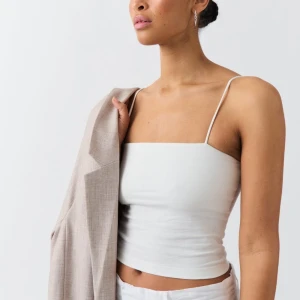 Vitt linne från Gina Tricot - Säljer en stilren vit linnetopp från Gina Tricot i storlek S. Toppen har smala axelband och en enkel design som passar perfekt till sommaren. Den är i mycket bra skick och kan enkelt matchas med olika outfits.