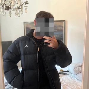 Svart dunjacka från Jordan - Säljer en snygg svart dunjacka från Jordan i mycket bra skick. Jackan har en dragkedja framtill och det ikoniska Jordan-logotypen på bröstet. Perfekt för kalla dagar och ger en sportig look. Passar både till vardags och mer avslappnade tillfällen.