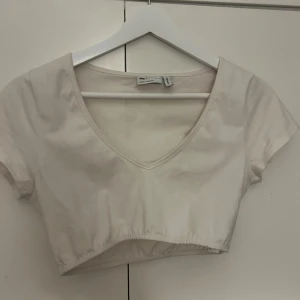 Vit croppad topp från asos - Säljer en vit croppad topp från asos i bomull. Den har en v-ringad design och korta ärmar, perfekt för sommardagar. Toppen är i bra skick och passar till både vardag och fest. Superfin att matcha med höga jeans eller kjol!