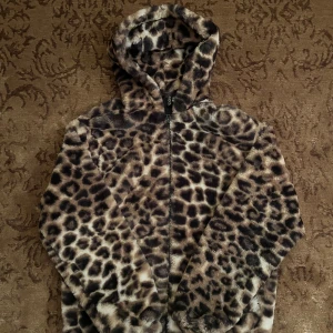 Leopardmönstrad pälsjacka med huva - Supercool leopardmönstrad pälsjacka från H&M med huva och dragkedja. Perfekt för att hålla sig varm och snygg under hösten och vintern. Jackan har en mjuk och fluffig känsla, vilket gör den både bekväm och trendig. Passar perfekt för en dag på stan eller en utekväll. 🐆✨