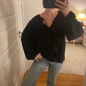 Svart blus med veckad design - Säljer en elegant svart blus med veckad design. Den har långa ärmar och en lös passform, perfekt för både vardag och fest. Blusen är i mycket bra skick och ger en stilren look. Storlek S 34💕