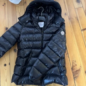 Svart dunjacka från Moncler - Säljer en snygg svart dunjacka från Moncler i mycket bra skick. Jackan har en glansig finish och är perfekt för kalla vinterdagar. Den har en dragkedja framtill och en avtagbar huva. Moncler-loggan syns på ärmen. Skicket är toppen! Köpte för ca ett år sen men säljer pga köpt en ny jacka Perfekt för både vardag och fest! Skriv vid frågor! (OBS: barn storlek: 164cm, motsvarar xs/s i vuxen storlek) kvitto och etiketter finns kvar (även triangeln som brukar sitter vid dragkedjan)💕💕🙏