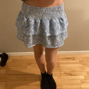 Blå blommig kjol från Gina Tricot - Superfin blå kortkjol från Gina Tricot med ett gulligt blommönster. Kjolen har en volangdetalj och är perfekt för sommardagar. Den är i mycket bra skick och har en elastisk midja för en bekväm passform. Perfekt för både vardag och fest! Använd 1 gång den har bara legat i garderoben. Ordinarie pris 250 men säljer för 100! Köpare står för frakt💕