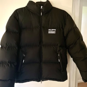 Svart pufferjacka från Axel Arigato - Säljer en snygg svart pufferjacka från Axel Arigato i storlek M. Jackan är gjord av återvunnen polyester och dun, perfekt för kalla dagar. Den har en dragkedja framtill och två praktiska fickor med dragkedjor. Jackan är lite traskg i högra arm/axel men inget som man tänker på eftersom det är lagat, perfekt för vintern! Nypris 4800 kr. Mitt pris 1999kr.