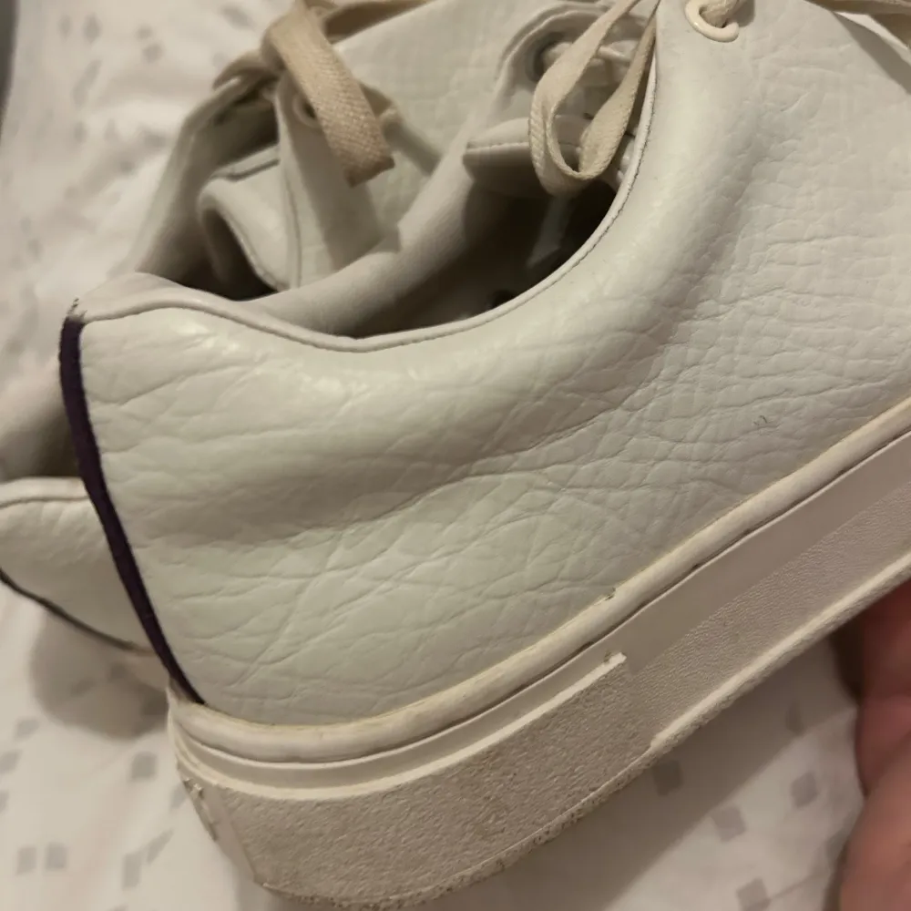 Säljer ett par vita sneakers i skinn med en cool lila rand på baksidan. De har snörning och en robust sula som ger bra stöd. Perfekta för vardagsbruk och passar till nästan allt i garderoben. Lite smuts på sulan men annars i bra skick. Sköna och stilrena! jag kommer också att tvätta dom innan dom skickas iväg! . Skor.