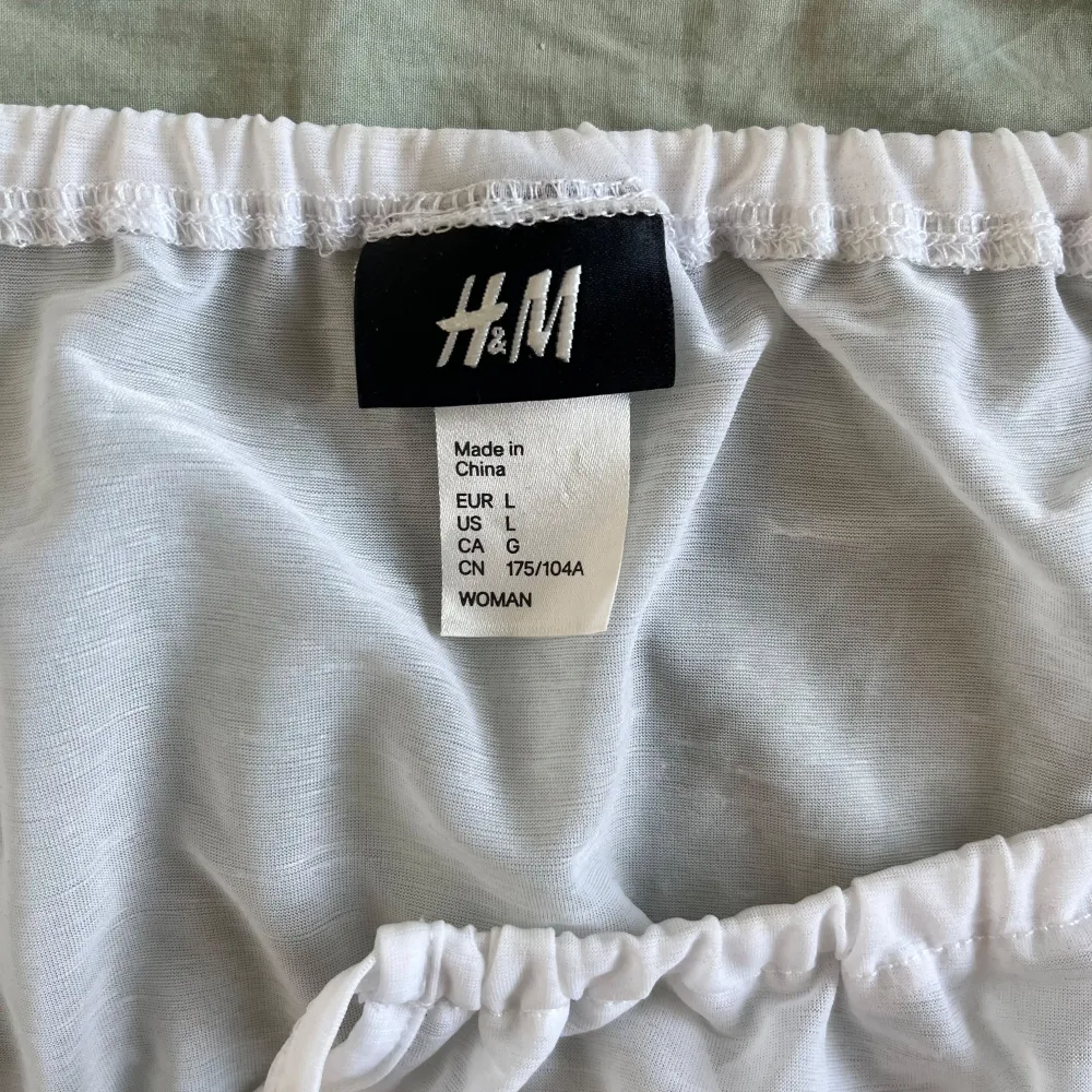 Säljer en söt vit blus från H&M i storlek L. Den har korta ärmar och en elastisk kant vid midjan för en bekväm passform. Perfekt för sommardagar eller en avslappnad vårlook. Blusen är i använt skick  och defekter syns på bilden ! 🌼. Toppar.