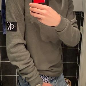 Grön tröja från Calvin Klein Jeans - Säljer en snygg grön tröja från Calvin Klein Jeans i storlek S passar även på M. Tröjan har en ribbad struktur och ett stilrent märke på ärmen. Perfekt för en casual look eller att mysa i hemma. Går att diskutera pris. Tröjan är i mycket bra skick då den inte har använts mycket.