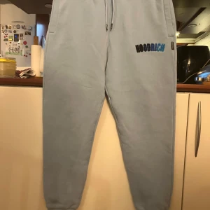 Ljusblå mjukisbyxor från Hoodrich - Säljer ett par ljusblå mjukisbyxor från Hoodrich i storlek XL. Byxorna har en bekväm passform med snörning i midjan och en cool logga på benet. Perfekta för en avslappnad stil eller chill dagar hemma. 🩵Säljer även matchande hoodie i storlek L.