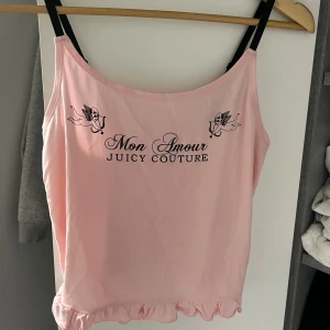 Rosa linne från Juicy Couture - Säljer ett supersött rosa linne från Juicy Couture med texten 'Mon Amour' och 'Sleeping Angel'. Det har svarta axelband och en volangkant längst ner. Perfekt för en avslappnad dag hemma eller som en del av en söt outfit. Helt nytt med taggar kvar!