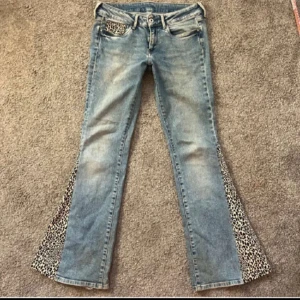 Blå jeans med leoparddetaljer - 💕Säljer ett par unika blå jeans med leopardmönstrade detaljer på fickor och längs benen. De har en bootcut-stil som ger en cool retrovibe. Perfekta för att sticka ut i mängden! Midjemått är 39cm och innerbenslängden är 79 cm! För mer info kontakta gärna mig 💕 🐆
