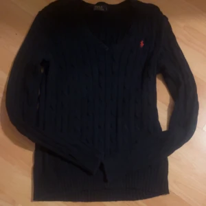 Mörkblå stickad tröja från Ralph Lauren - Säljer en snygg mörkblå stickad tröja från Ralph Lauren med v-ringning och det klassiska röda logotypen på bröstet.