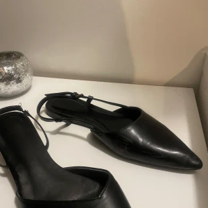 Svarta spetsiga ballerinaskor - Snygga svarta ballerinaskor i skinn med spetsig tå och smala remmar. Perfekta för både vardag och fest. De har en elegant och stilren design som passar till många olika outfits.