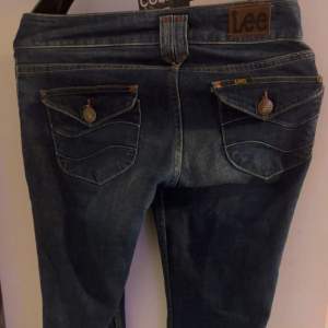 Säljer ett par snygga blå jeans från Lee i bra skick.(dock är lite slitet längst ner.) De har en klassisk femficksdesign med knappar och dragkedja fram. Jeansen har en bootcut-stil som ger en skön retrovibe. Perfekta för både vardag och fest!