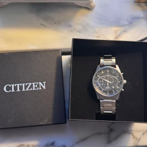 Citizen herrklocka i silver - Säljer en snygg Citizen herrklocka i silver med svart urtavla och flera små urtavlor för extra funktioner. Klockan har en robust metallarmband och är i mycket bra skick. Perfekt för både vardag och fest! Ord pris 2200