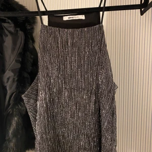 Glittrig topp från Gina Tricot - Snygg glittrig topp från Gina Tricot i svart och silver. Perfekt för festliga tillfällen med sin ärmlösa design och smala axelband.  Toppen har en elegant och modern look som passar perfekt för nyår eller andra speciella tillfällen.