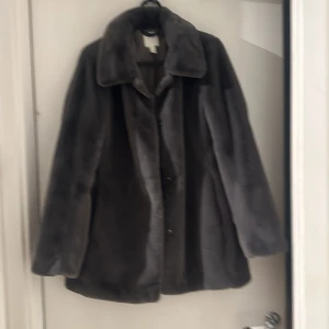 Grå pälsjacka från H&M - Säljer en supermjuk och stilren grå pälsjacka från H&M i storlek XS. Perfekt för kyliga höst- och vinterdagar. Jackan har en klassisk krage och knappar framtill. Den är i mycket bra skick och redo för nya äventyr! 🐻