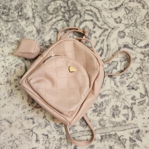 Rosa quiltad ryggsäck med hjärtdetalj - Säljer en superfin litem rosa ryggsäck. Den har en söt hjärtdetalj i guld på framsidan och innejåller ocksä en mini väska för kanske airpods? 💕