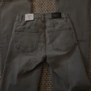 Grå bootcut jeans från Gina Tricot - Säljer ett par snygga ljusgrå bootcut jeans från Gina Tricot i storlek 32. De är lågmidjade och har en klassisk femficksdesign. Perfekta för en avslappnad men stilren look. Helt nya med tag kvar!