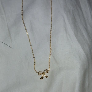 Guldhalsband med rosett - Säljer ett elegant guldhalsband med en söt liten rosett som hänge. Perfekt för att ge en extra touch till din outfit, oavsett om det är till vardags eller fest. Kedjan är tunn och smidig, vilket gör den bekväm att bära hela dagen. Ett måste för alla som älskar stilrena smycken!