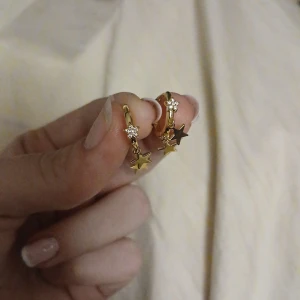Guldörhängen med stjärnor och stenar - Säljer ett par superfina guldörhängen med hängande stjärnor och gnistrande stenar. Perfekta för att ge lite extra bling till din outfit! De är i mycket bra skick och passar både till vardag och fest. ✨