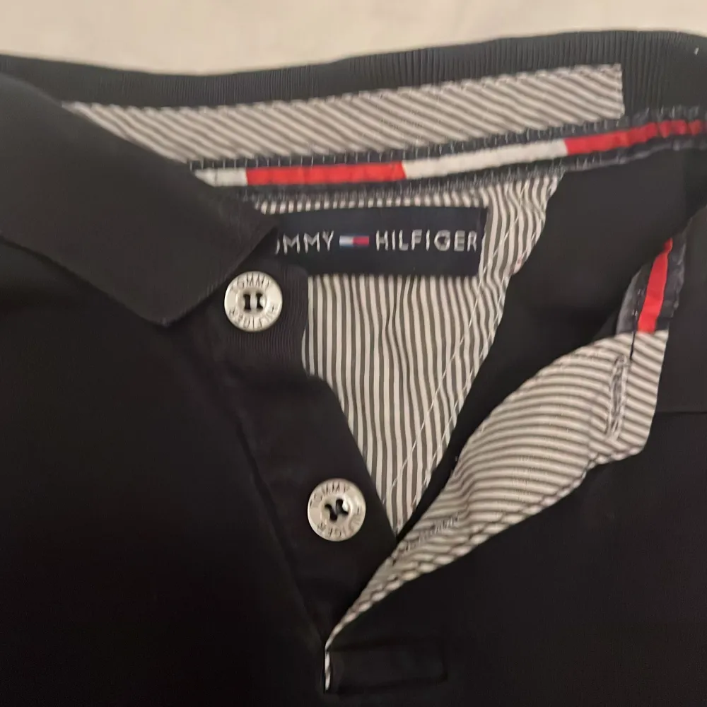 Säljer en stilren marinblå långärmad pikétröja från Tommy Hilfiger. Den har klassiska knappar och en snygg randig detalj på insidan av kragen. Tröjan är i använt skick och ev lite urtvättad. Ca stl 150-160. Tröjor & Koftor.