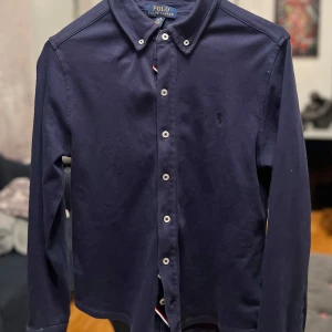 Mörkblå skjorta från Ralph Lauren - Säljer en snygg mörkblå skjorta från Ralph Lauren i storlek 10-12 år . Skjortan har långa ärmar och klassiska knappar framtill. Perfekt för både vardag och festliga tillfällen. Den är i mycket bra skick och gjord av bomull för en bekväm passform. Hund i hemmet.