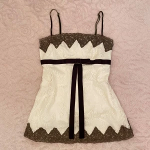 Vitt spetslinne med mörkbrun rosett🎀 - Super gulligt vitt linne med spets och mörkbruna detaljer från märket ”la petite française”. Den är i gott skick och passar storlek S.💗