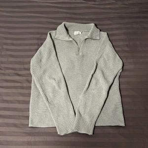 Grå stickad tröja från East West - Säljer en stilren grå stickad tröja från East West. Den har en dragkedja framtill och en klassisk krage. Perfekt för kyliga dagar och passar både till vardags och lite finare tillfällen. Tröjan är i mycket bra skick och redo för en ny ägare! 