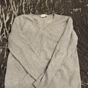 Grå tröja från VILA - Säljer en stilren grå tröja från VILA i storlek XL. Tröjan har en v-ringad design och är perfekt för både vardag och lite finare tillfällen. Den är långärmad och har ribbade muddar vid ärmslut och nederkant. Supermjuk och bekväm!
