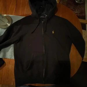 Svart zip hoodie från Polo Ralph Lauren - Säljer en svart zip hoodie från Polo Ralph Lauren i storlek M. Den har en dragkedja framtill och en mysig huva med ett snyggt rutigt mönster på insidan. Perfekt skick